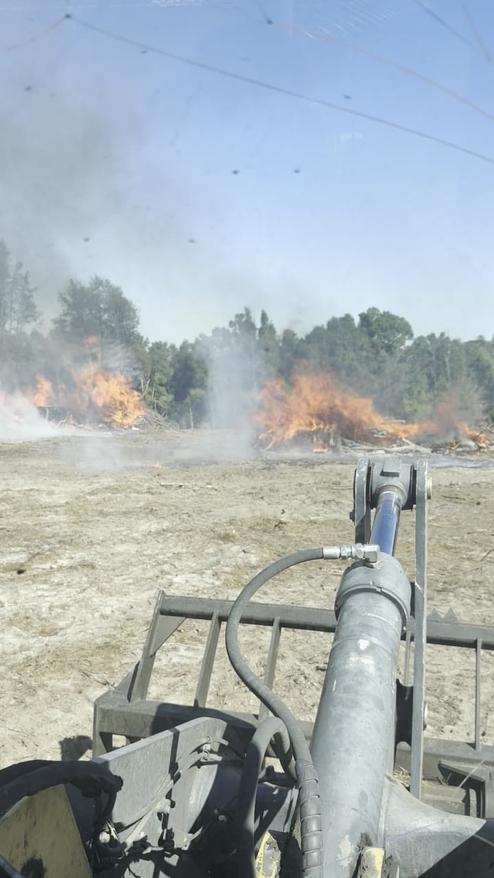 Burning brush piles on a freshly cleared tract, seen from the skid steer